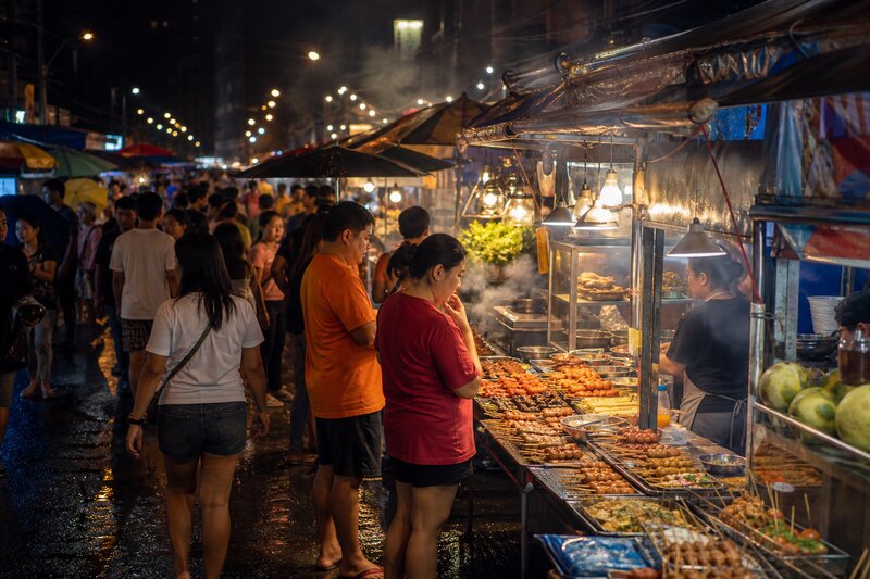 A busy night market crowd browsing brightly lit stalls after dark, warm lights reflecting off the pavement